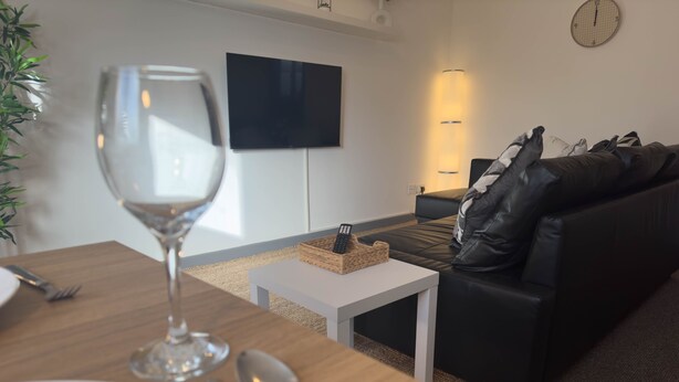 Ein modernes Wohnzimmer mit einem Holzespeisetisch, einem Weinglas und einem schwarzen Ledersofa.