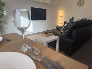 Een moderne woonkamer met een houten eettafel, een glas wijn en een zwarte leren bank.