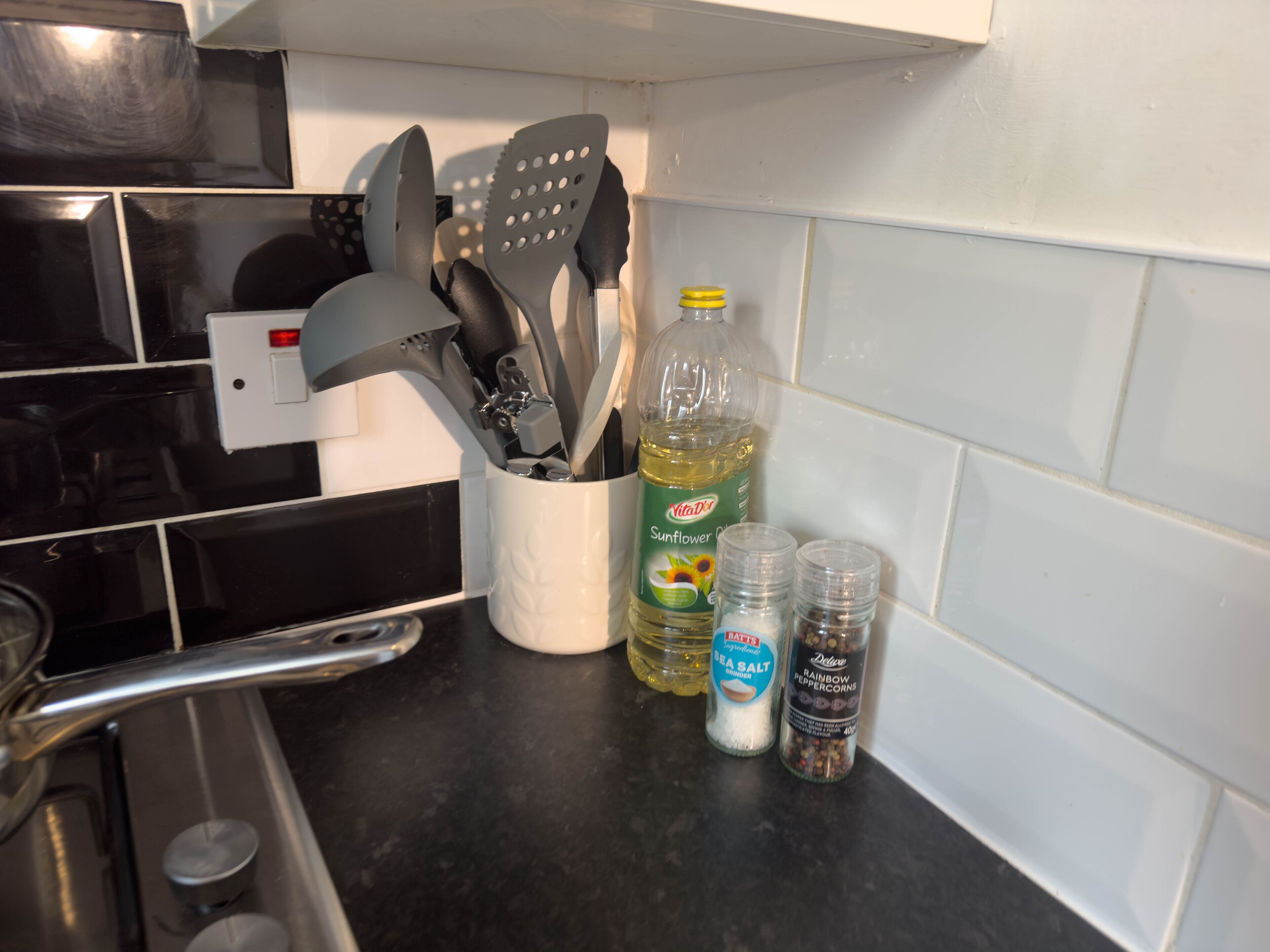 Una encimera de cocina con diversos utensilios, una botella de aceite y recipientes de sal y pimienta.