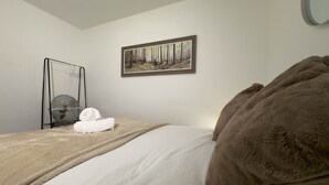 Ein Hotelzimmer mit Bett, Decke, Handtuch, einem Bild an der Wand und einem Standventilator.