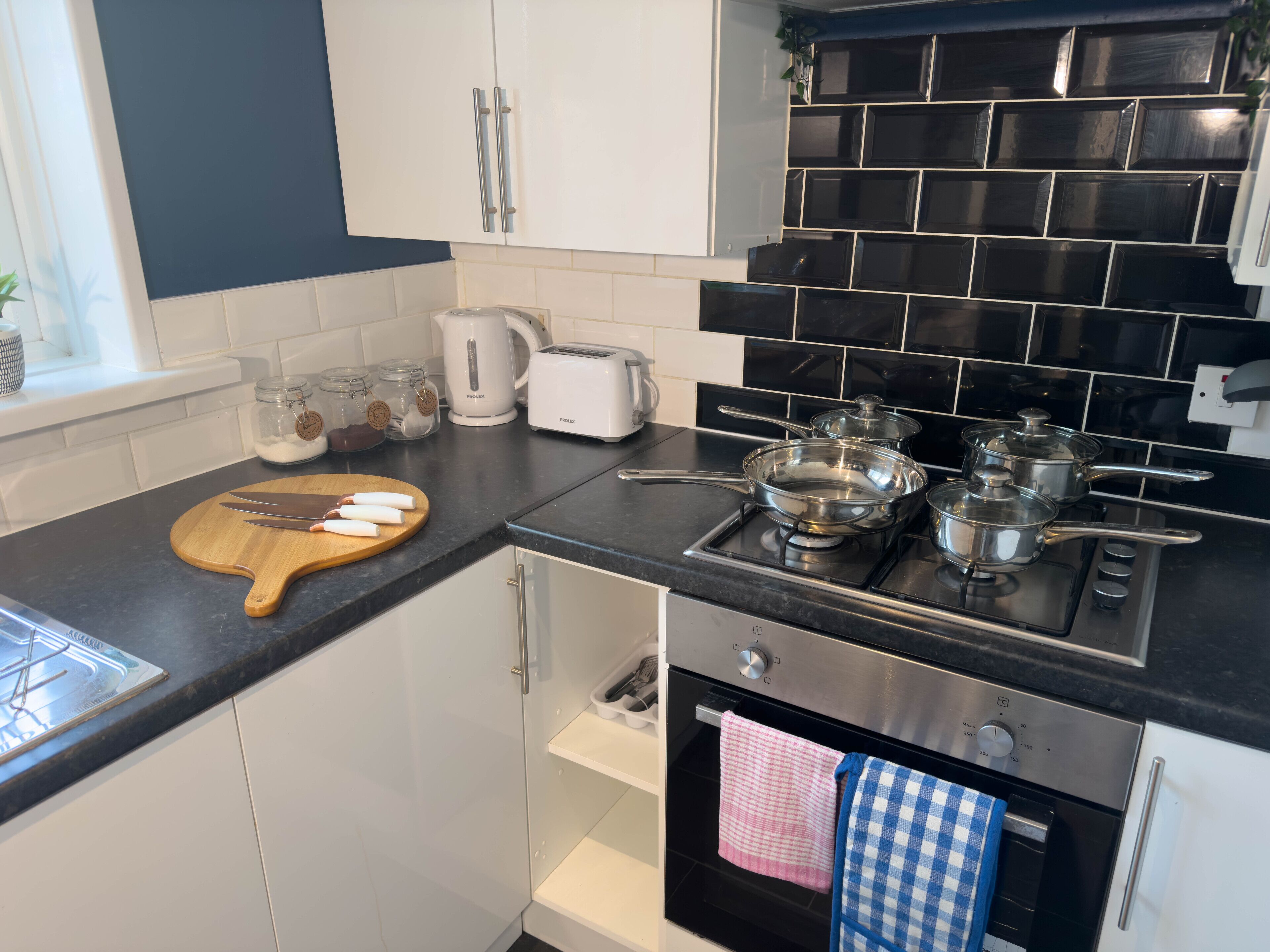 A modern kitchen with white cabinets, a black countertop, a stove, and an oven.