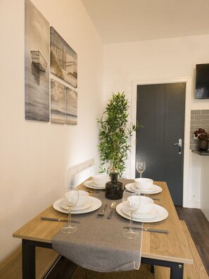 A dining table set with plates, glasses, and cutlery, a potted plant, and a grey throw on the table. - Principality Suites (1 bed) (Cardiff)