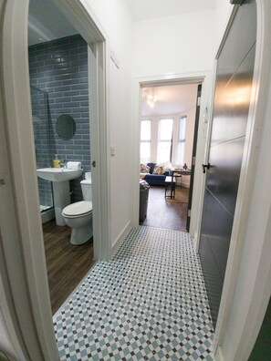 A hallway with a checkered floor leading to a bathroom with a sink and toilet. - Principality Suites (1 bed) (Cardiff)