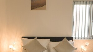 Een opgemaakt bed met witte lakens en kussens, een gebreid plaid en nachtlampjes.