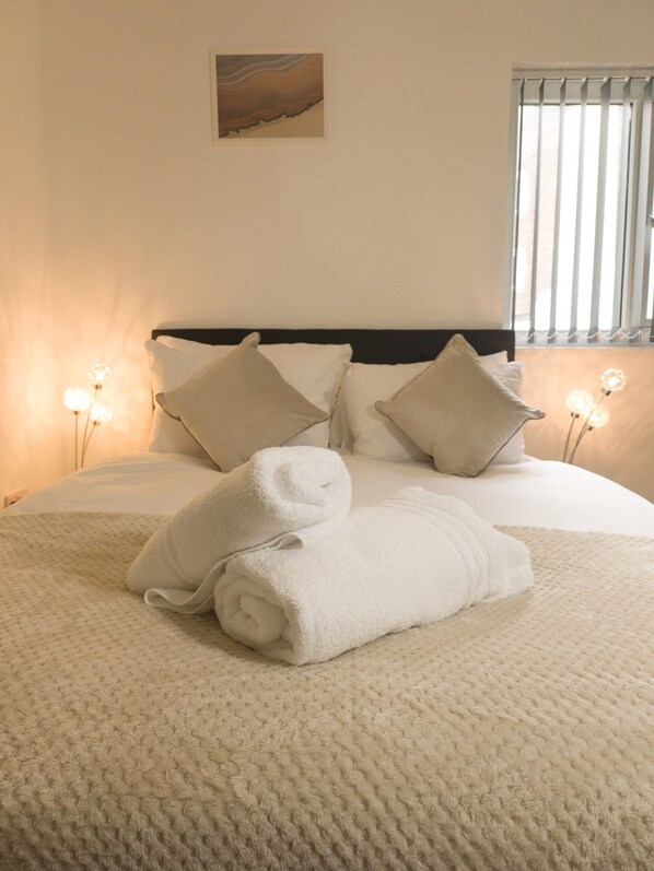 A neatly made bed with white linens and pillows, a textured blanket, and bedside lamps. - Principality Suites (1 bed) (Cardiff)