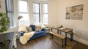 Een moderne woonkamer met een blauwe bank, een eettafel gedekt voor vier personen, en grote ramen.
