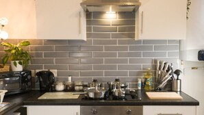 Een moderne keuken met witte kasten, een zwart aanrecht en een grijze betegelde achterwand. Op de kasten staan planten, er is een koffiezetapparaat en diverse keukengerei.