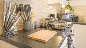 Una cucina con piano di lavoro nero, utensili in acciaio inossidabile, tagliere di legno e diverse pentole e padelle.