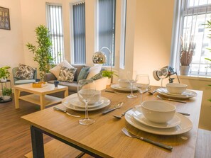A dining area with a table set for four, a sofa, a coffee table, and a potted plant. - Principality Suites (3 beds) (Cardiff)