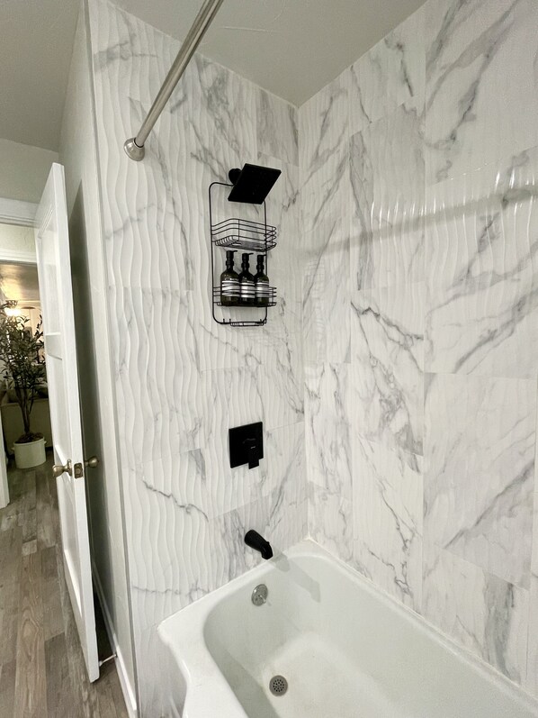 A bathroom with a marble wall, a shower with a glass door, and a bathtub.