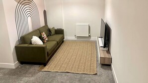 Una sala moderna con sofá, alfombra, radiador y televisor.