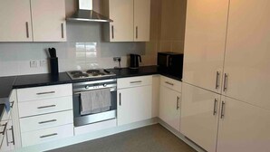 Una cocina moderna con armarios blancos, estufa de acero inoxidable y encimera negra.