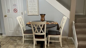 A dining area with a round table, four chairs, a ceiling fan, and a wall-mounted sign. - The Blue Door Cottage  (Dundee)