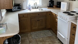 A kitchen with wooden cabinets, a white stove, a sink, and a window with lace curtains. - The Blue Door Cottage  (Dundee)