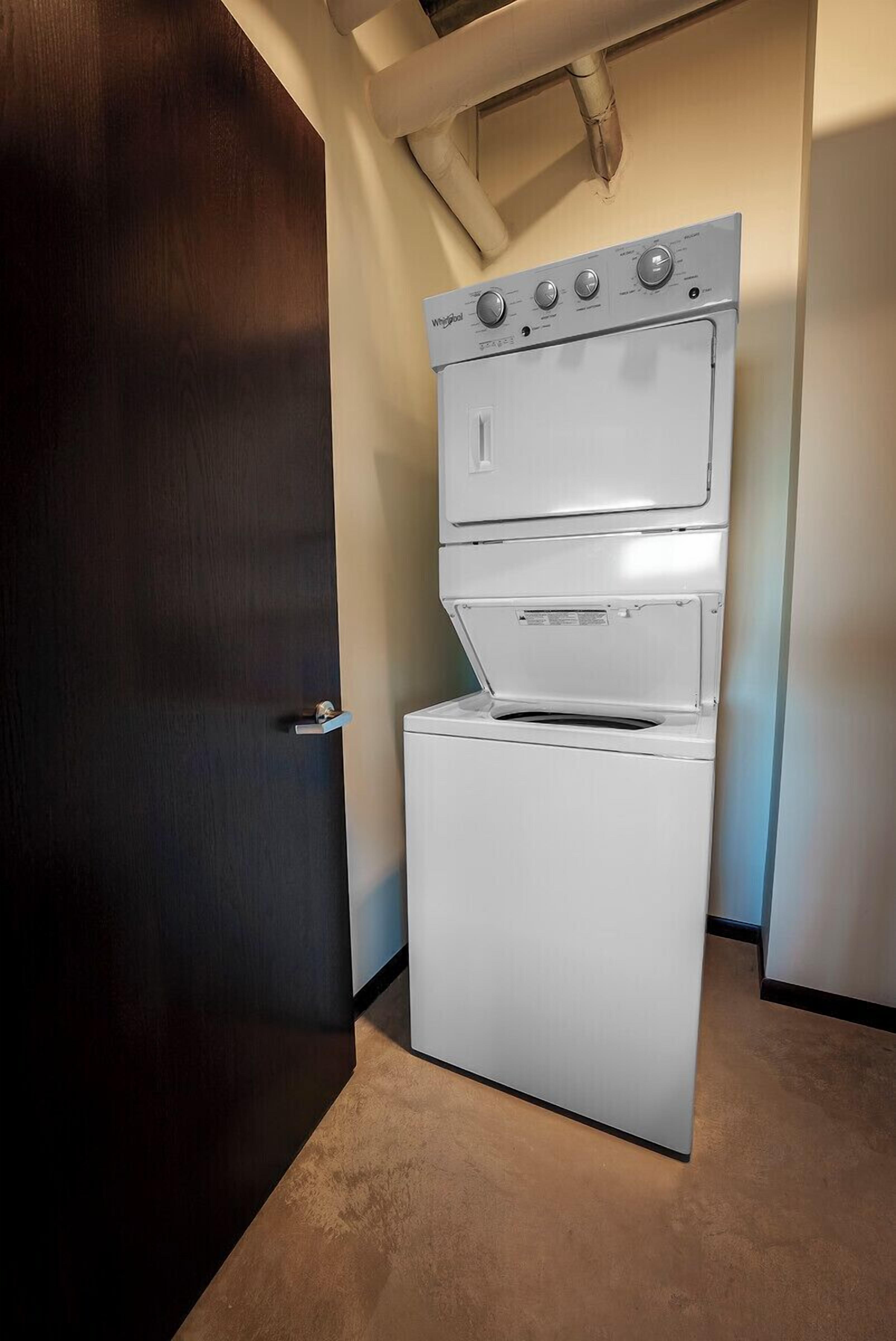 A compact laundry room with a stacked washer and dryer, a door, and a ceiling vent.