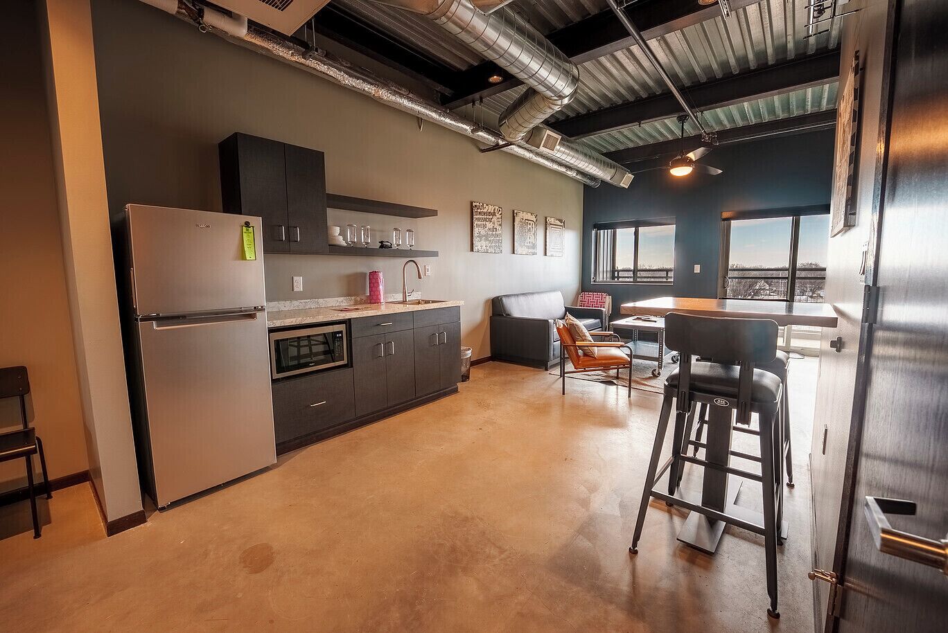 Eine moderne Küche mit Edelstahl-Kühlschrank, integriertem Backofen und Mikrowelle. Eine Bar mit Hockern und ein großes Fenster bieten Blick auf die Stadt.
