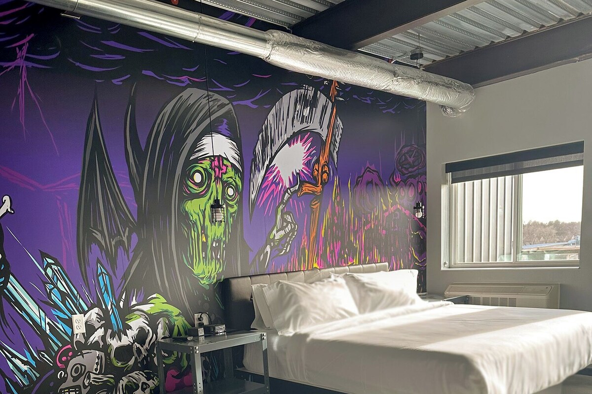 A bedroom with a bed, a couch, a wall mural, and a window.