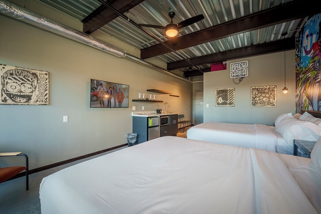 A room with two beds, a kitchenette, and artwork on the walls.