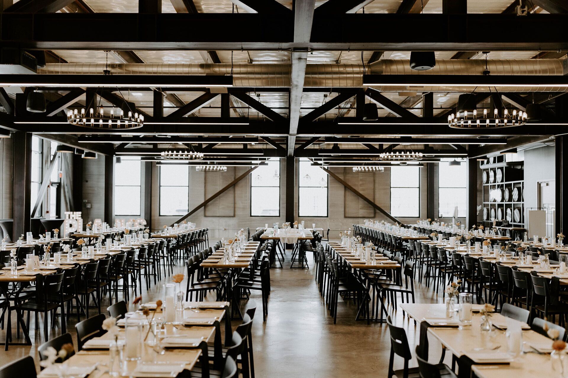 Une vaste salle à manger, dotée de nombreuses tables dressées pour le repas, de grandes fenêtres et d’un plafond haut avec des poutres apparentes.