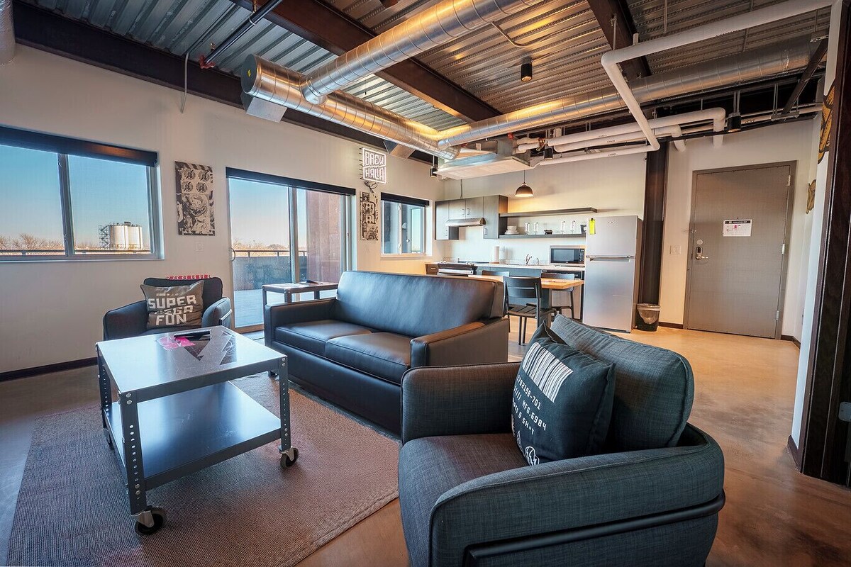 A modern living room with a sofa, a coffee table, and a cart. There is a kitchen in the background with a microwave and refrigerator.