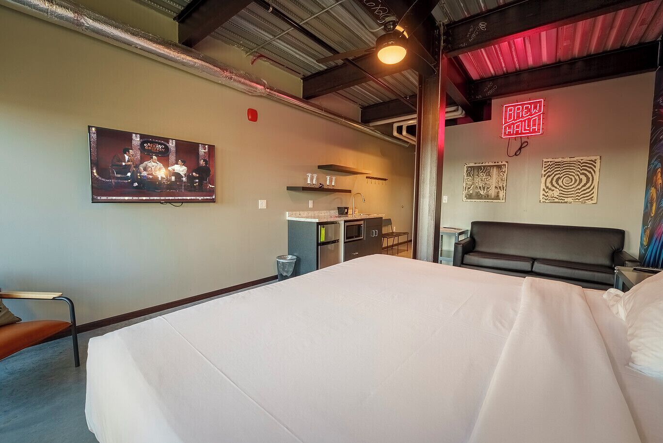 Een hotelkamer met een bed, een aan de muur bevestigde televisie, een kitchenette en een neonreclame.