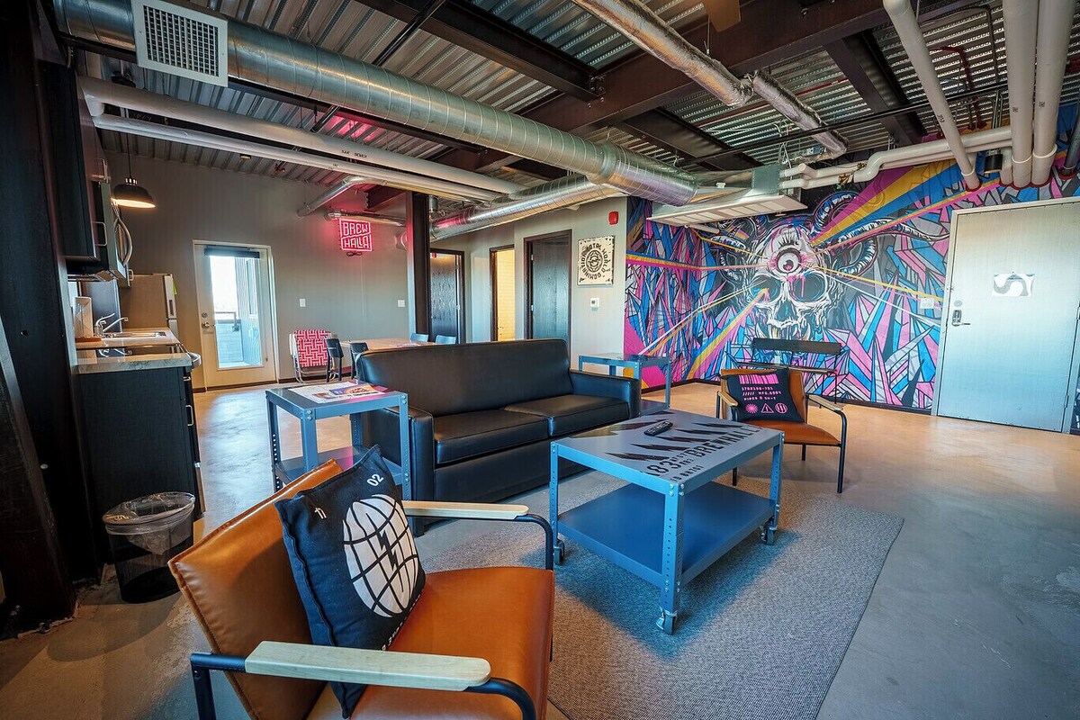 A modern lounge area with a sofa, armchairs, a coffee table, and a colorful mural.
