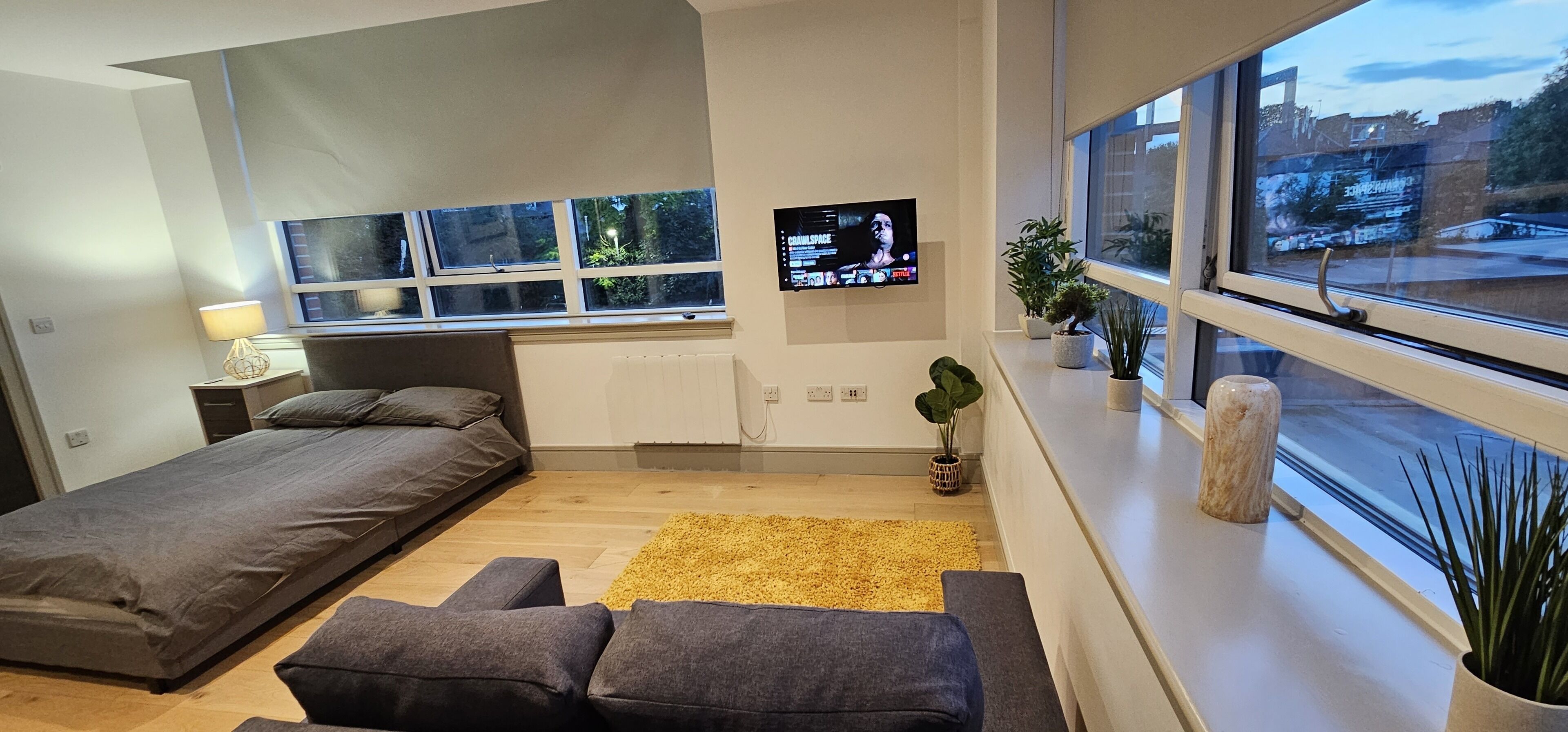 A modern bedroom with a bed, a sofa, a TV, and a window with a view of the street.