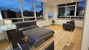 Une chambre à coucher moderne avec un lit, un bureau, une chaise et un téléviseur posé sur une étagère.