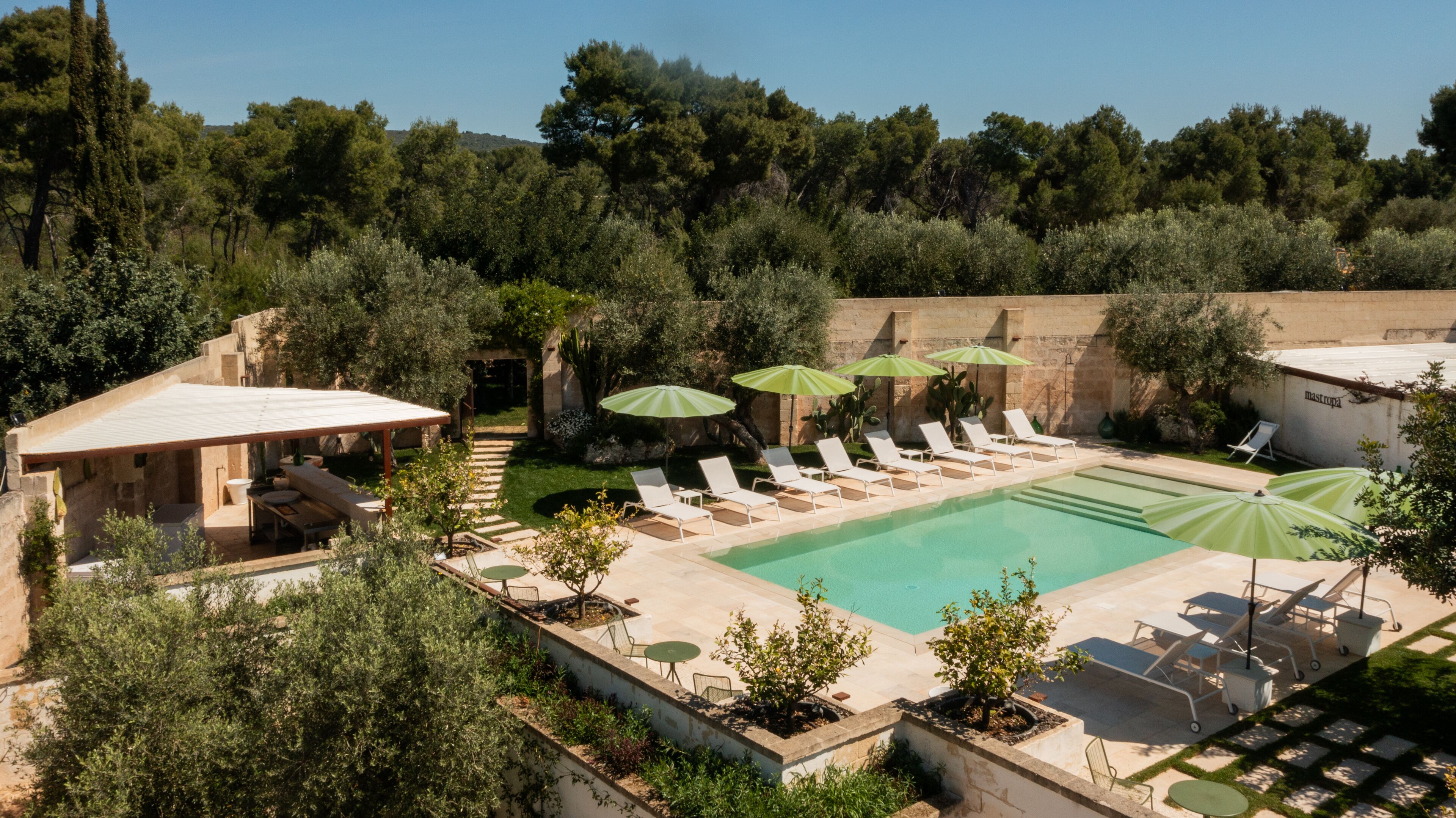 A pool area with lounge chairs and umbrellas, surrounded by greenery and stone structures.