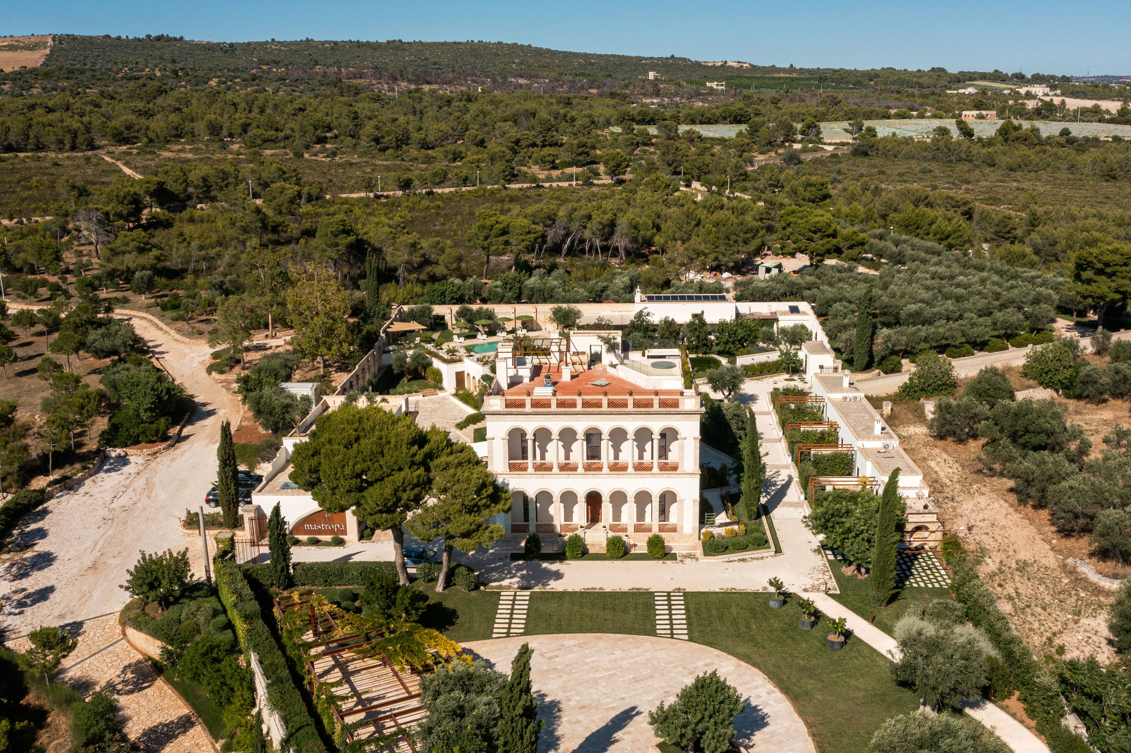 Vue aérienne d’un bâtiment historique doté d’une cour intérieure, entouré d’une végétation luxuriante et d’oliviers.