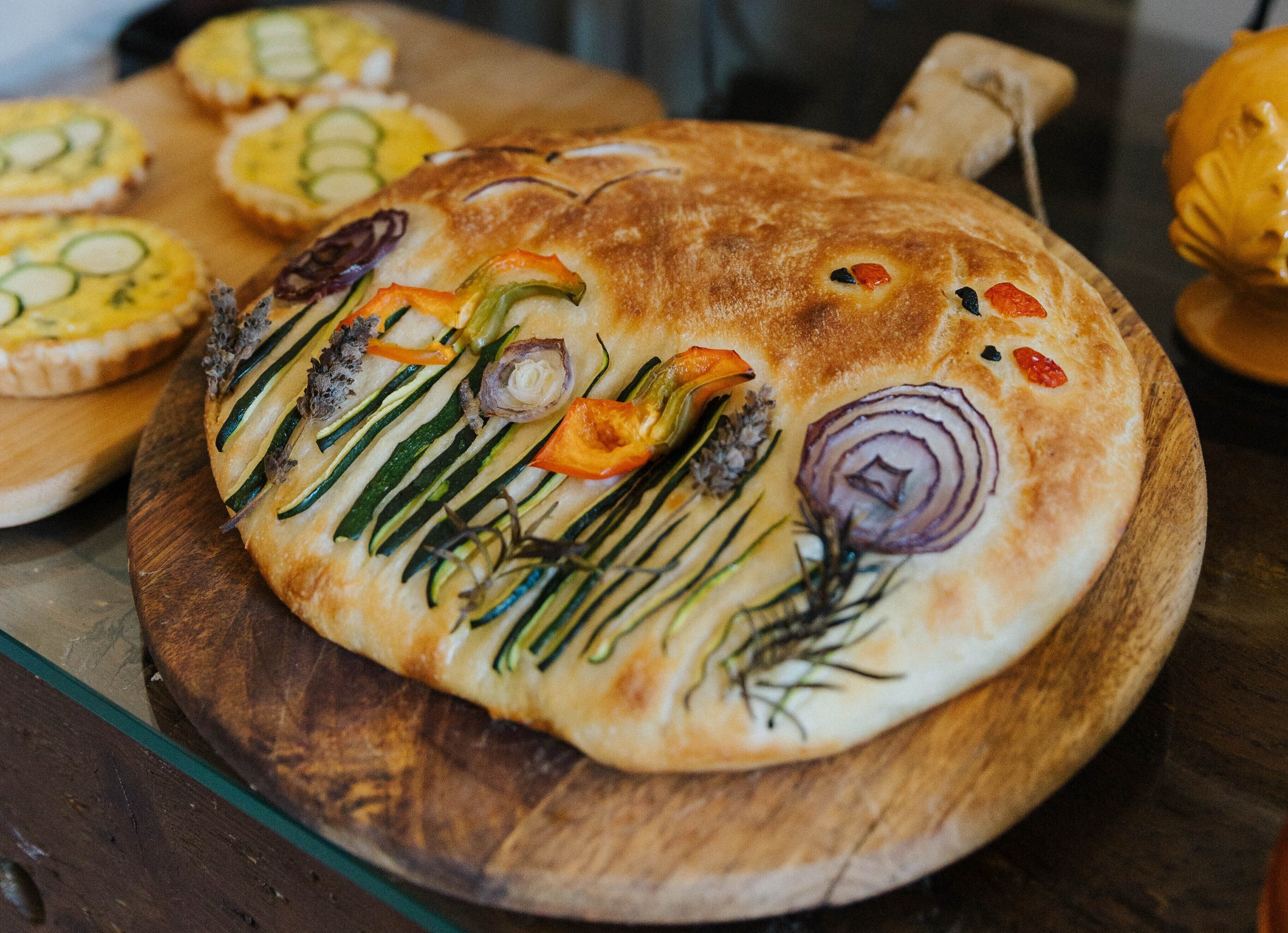 Een plat, rond brood belegd met groenteverkrachtingen op een houten plank.
