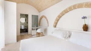 Un dormitorio con una cama grande, un escritorio y un baño visible a través de un arco.