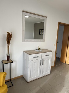 A modern room with a white cabinet, a mirror, and a small table with a vase of dried plants. - Sunset Apartment mit Rheinblick in Urbar (Urbar)