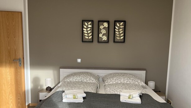 A bedroom with a large bed, a wooden door, and three wall-mounted leaf decorations. - Sunset Apartment mit Rheinblick in Urbar (Urbar)