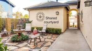 A shared courtyard with a stone fountain, seating area, and a wall with a decorative emblem.
