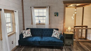 Una habitación acogedora con un sofá azul, un escritorio de madera y una ventana con cortinas.