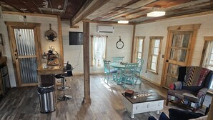 Un interior rústico con pisos de madera, una zona de comedor con sillas azules, una estación de café y un sillón estampado.