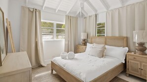Un dormitorio con cama de madera, ropa de cama blanca, ventilador de techo y vistas al exterior.