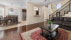 A spacious living room with a dark leather couch, a wooden coffee table, and a red patterned rug. A dining area with a wooden table and chairs is visible in the background. - Secluded Luxe Home | Private Pool & Grill (Allen)