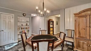 Uma sala de jantar com uma mesa redonda, seis cadeiras, um candelabro, uma estante e um armário de madeira.