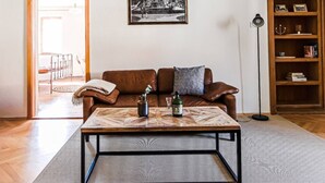 Een ruime woonkamer met een houten vloer, een bruine leren bank, een salontafel en een boekenkast.