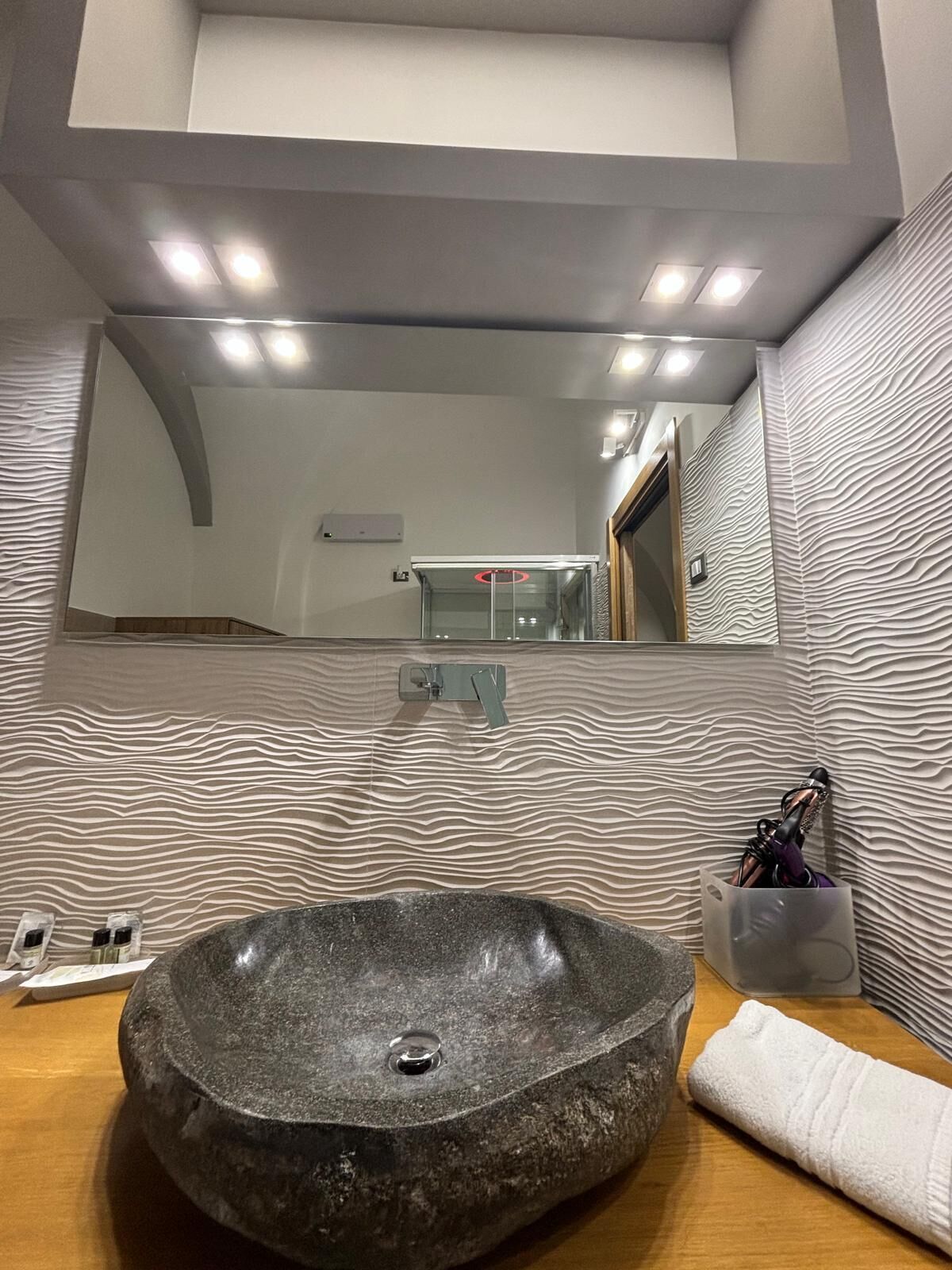 A bathroom with a large oval sink, a mirror, and a textured wall.