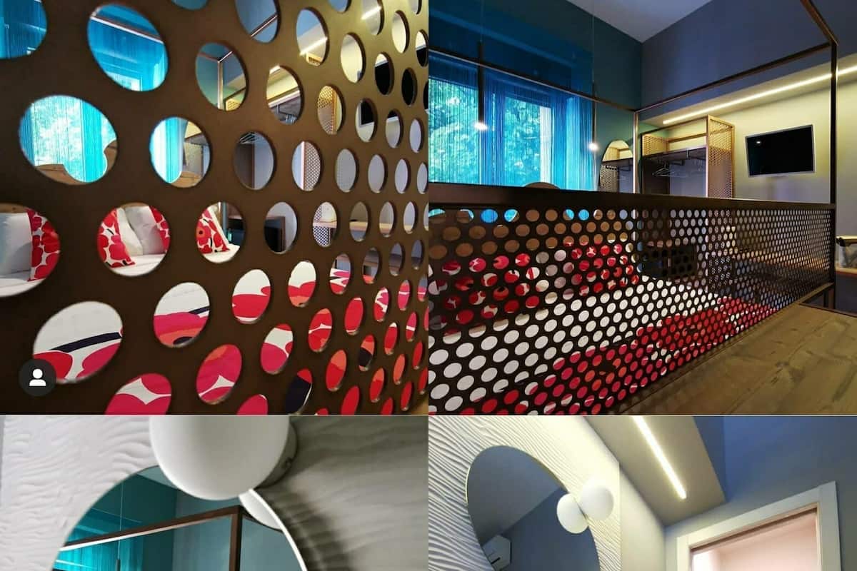 Ein modernes Hotelzimmer mit großem Fenster, einer dekorativen Lochwand, einem runden Spiegel und einem Badezimmer mit Steinwaschbecken und Dusche.