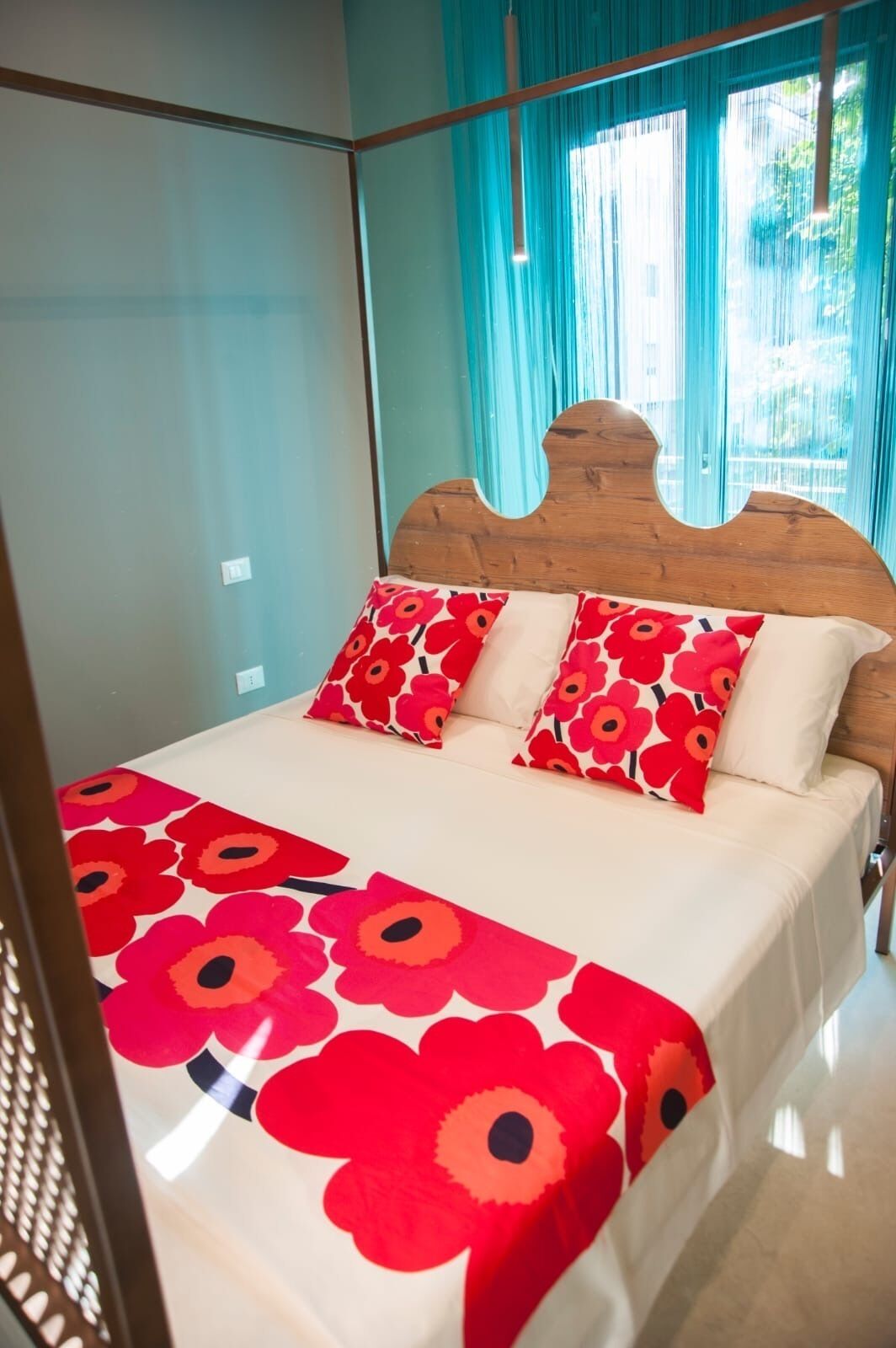 A bed with a wooden headboard, two red floral pillows, and a white bedspread with red floral patterns.