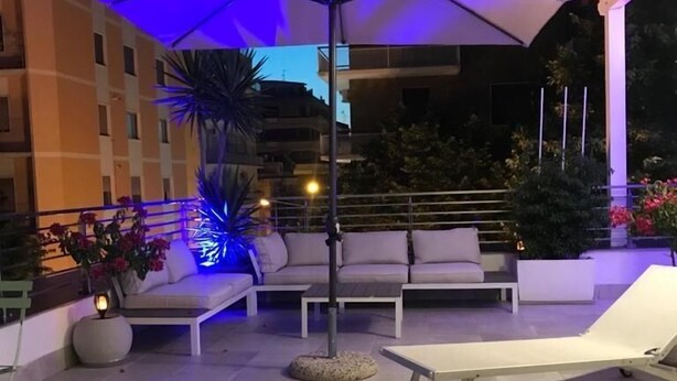 An outdoor patio area with a white sofa, a lounge chair, and a large umbrella providing shade. - B&B del corso foggia (Foggia)