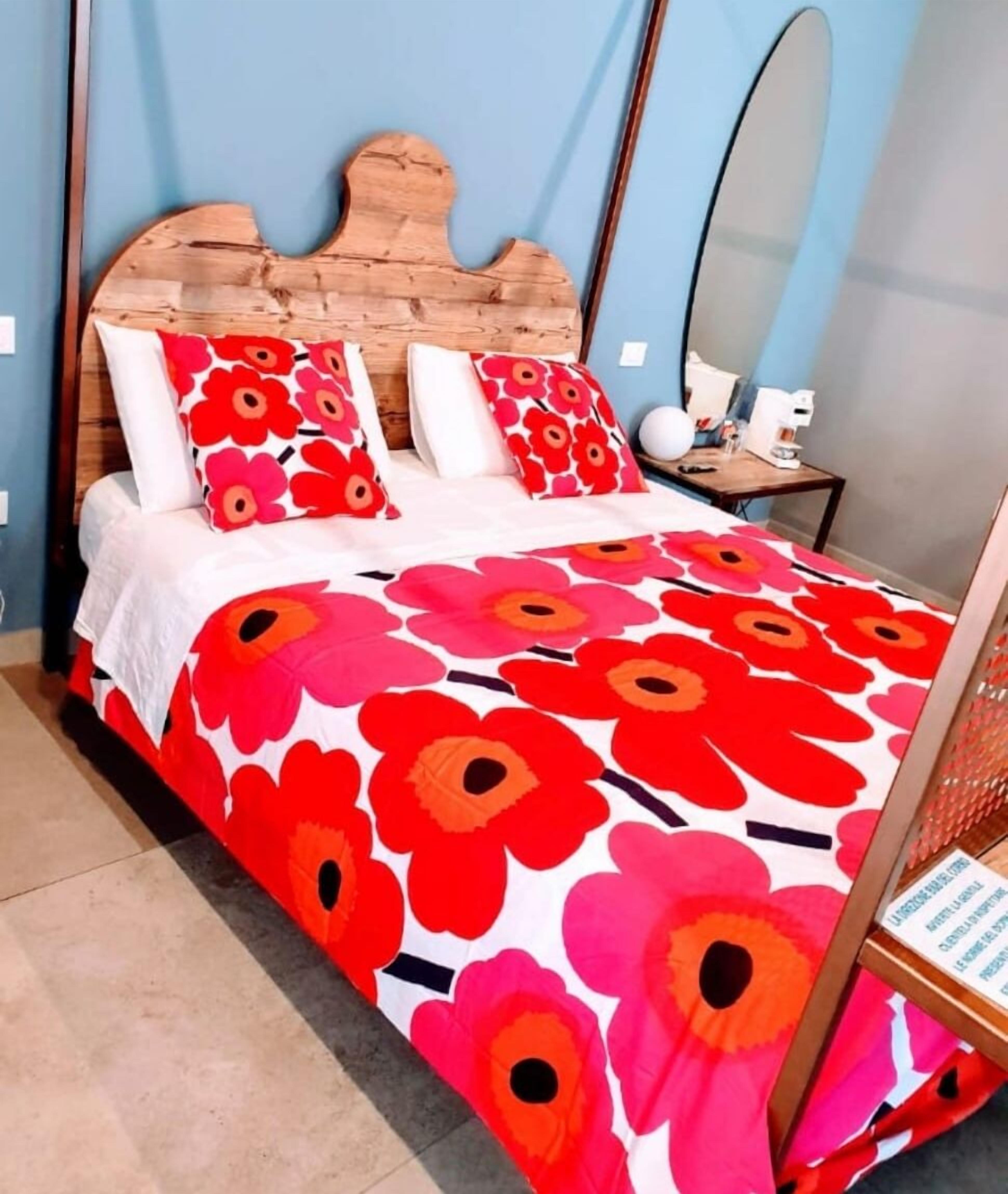 A bed with a wooden headboard, red and white floral bedding, and a small bedside table with a lamp.