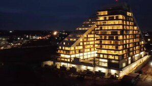 A multi-story hotel with a distinctive pyramid-like structure, illuminated windows, and a flat roof. - Immaculate Beauty Gem-5 Star Location- Pools - Gym (Accra)