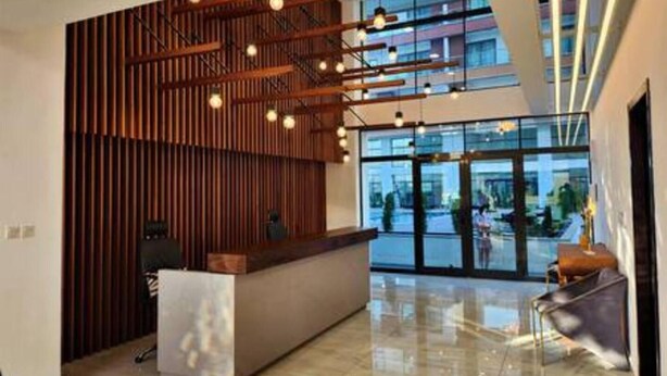 A modern reception area with a wooden slat wall, a reception desk, and a glass entrance. - Immaculate Beauty Gem-5 Star Location- Pools - Gym (Accra)