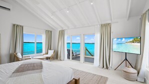 A bedroom with a large bed, a TV, and a view of the ocean. - Overwater Bungalow at Georgetown (Exuma)