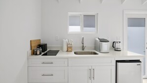 A modern kitchen with white cabinets, a stainless steel sink, a window above the sink, and a refrigerator. - Overwater Bungalow at Georgetown (Exuma)